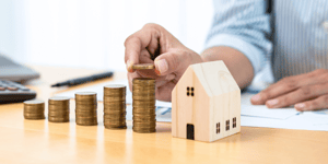 Coins being stacked next to a wooden model of a house